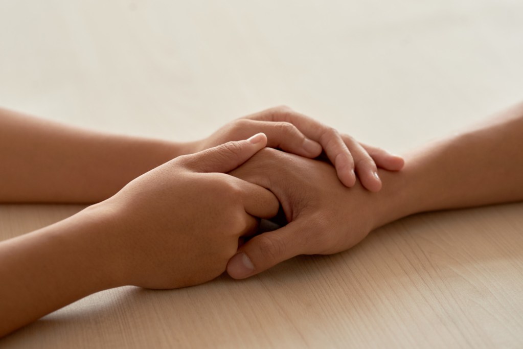 Une main tenue délicatement entre les deux mains d'une autre personne en signe de réconfort.